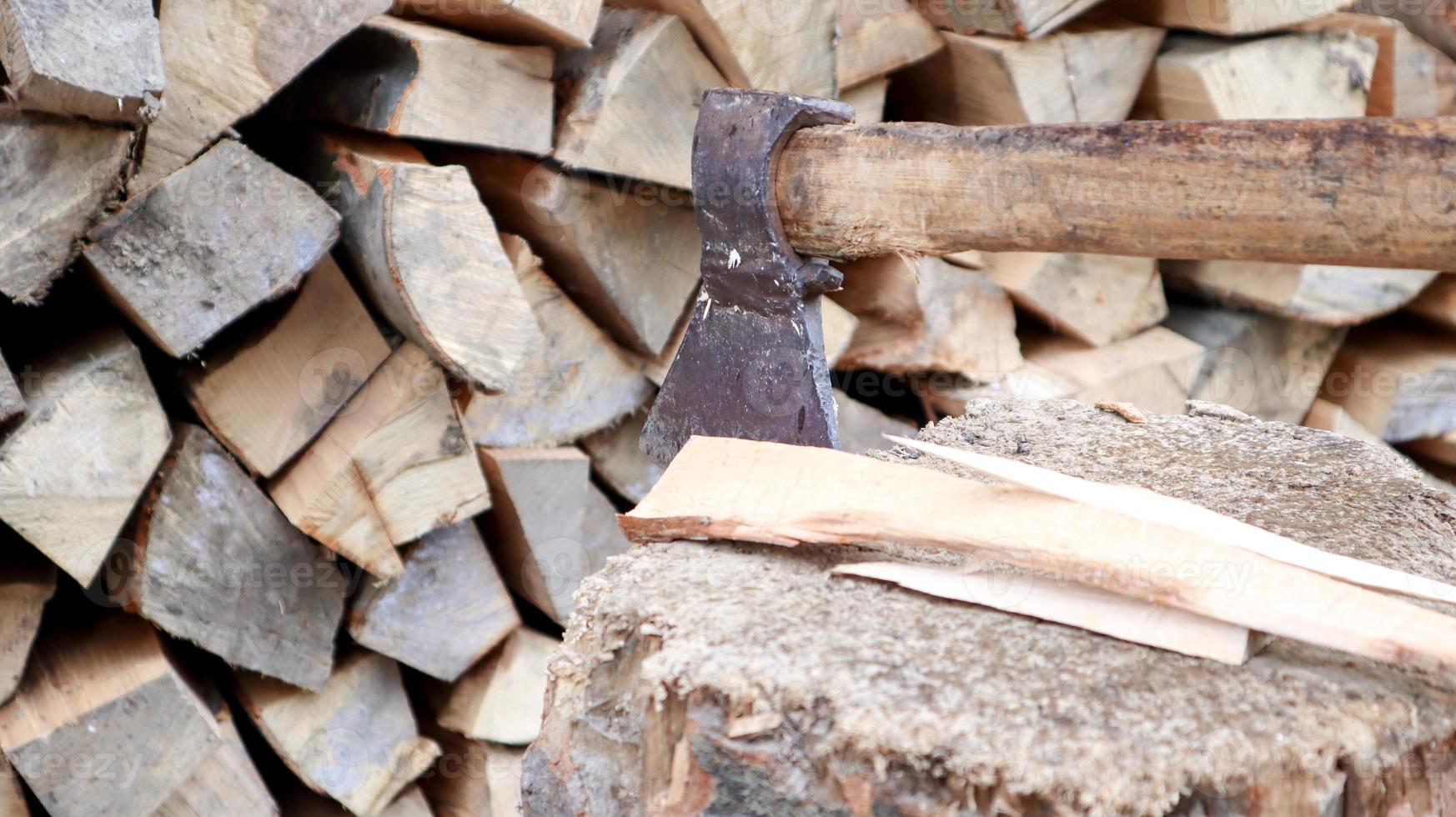 versnipperd brandhout voor de winter voor verwarming. de bijl wordt met een mes in de stronk gestoken. hakmes met een houten handvat. oogsten op de boerderij. droog brandhout gestapeld in stapels voor het verwarmen van een huis foto