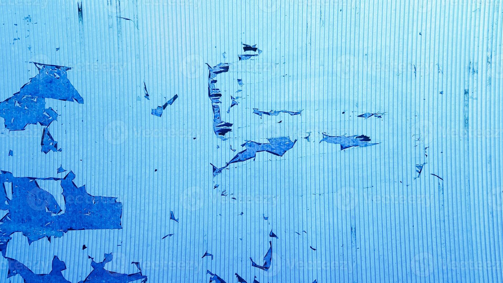 ongelijk golvend plastic oppervlak met de overblijfselen van schilferige film en papier. abstracte verouderde blauwe achtergrond. kopieer ruimte, ontwerp. graan blauwe verf muur achtergrond of textuur foto