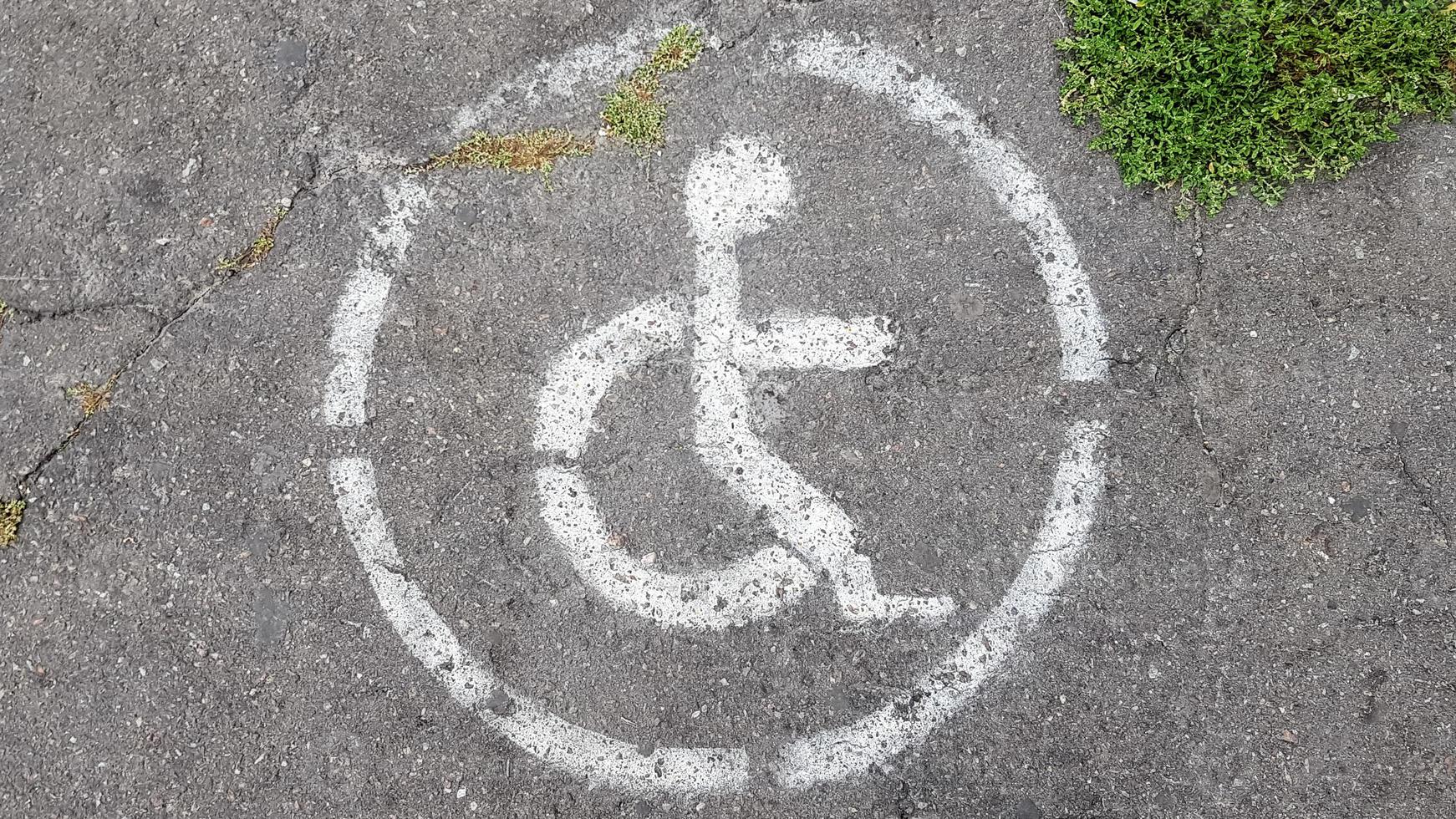 gehandicaptenparkeerplaats symbool. gehandicapte baai gemarkeerd met een persoon in een rolstoelbord op grijs asfalt op een grote parkeerplaats close-up. uitzicht van boven foto