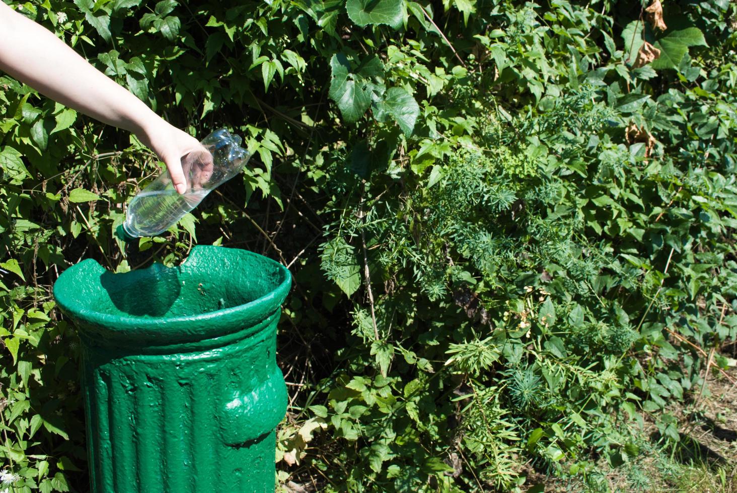 wijsvinger Rondlopen samenvoegen vrouwelijke hand gooit een plastic fles in een kleine ijzeren prullenbak in  een groen park in de zomer, close-up. natuurbescherming tegen plastic.  4538137 Stockfoto