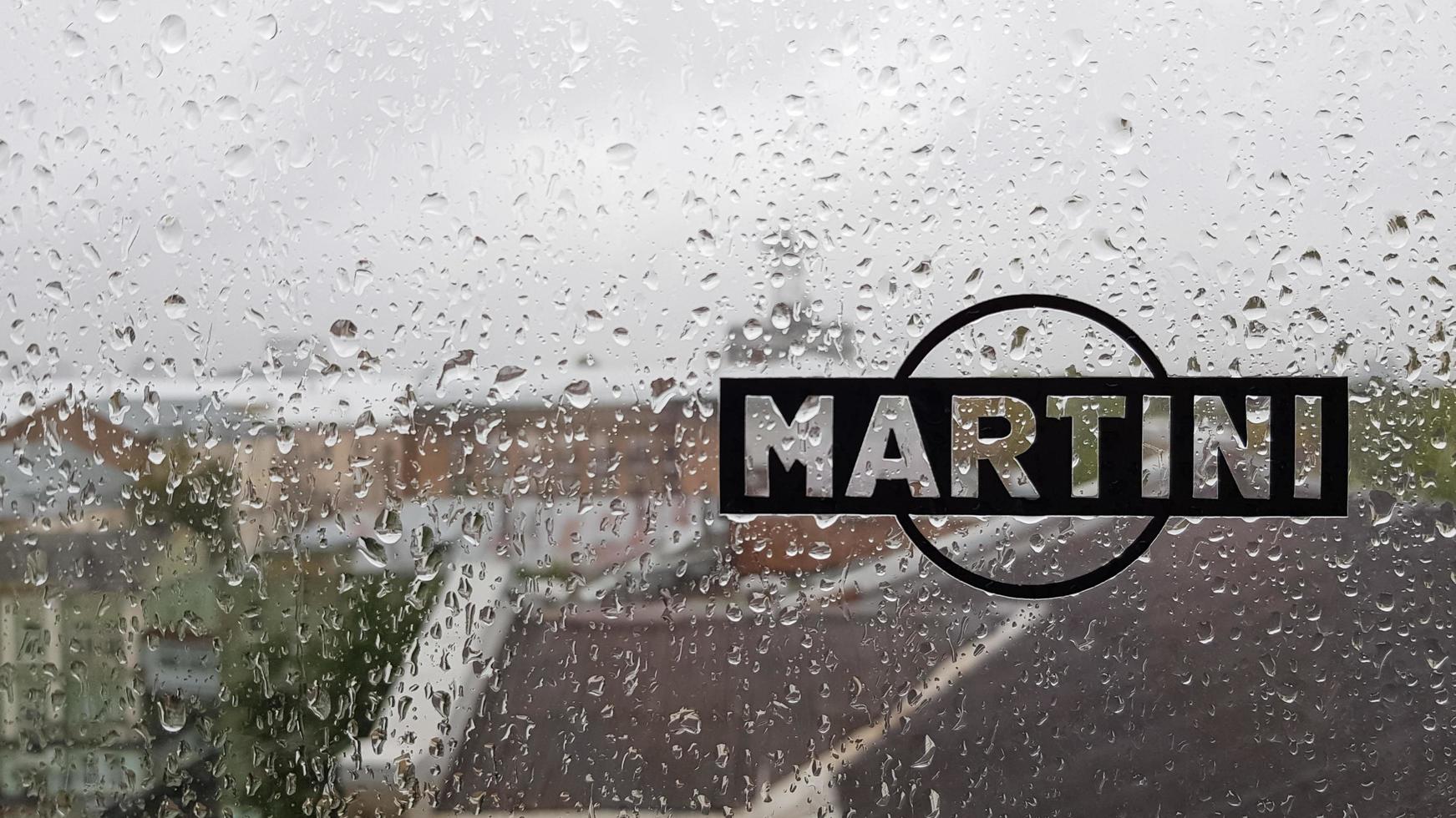 martini sticker-logo. een merk van in Italië gemaakte vermouths en mousserende wijnen. waterdruppel op glazen raam tijdens regen met onscherpe achtergrond van stadsscène. Italië, Turijn - 1 oktober 2020. foto