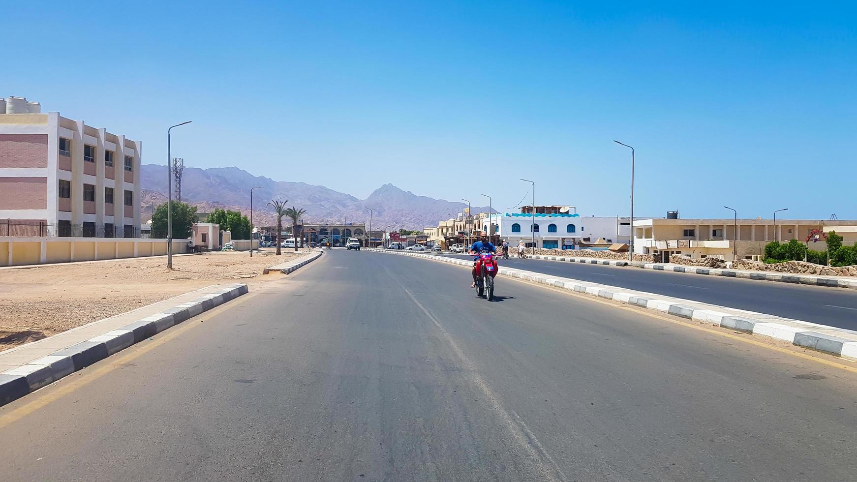 egypte, dahab - 20 juni 2019. een arabier rijdt op een scooter langs een van de straten van dahab. woestijn straat. Egyptische woongebouwen. de stad dahab. foto