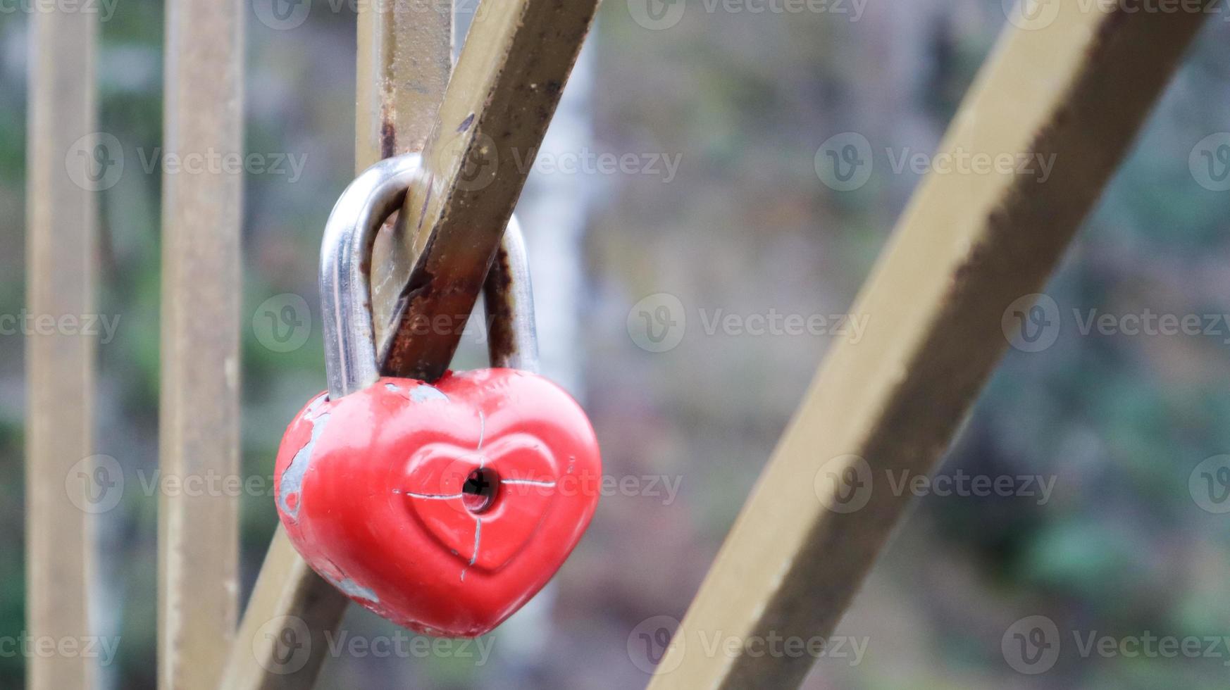 armoedig rood slot in de vorm van een hart. Valentijnsdag liefde concept. een hangslot dat aan een metalen balustrade hangt, is een teken van eeuwige liefde. de traditie om een kasteel aan een hek te haken foto