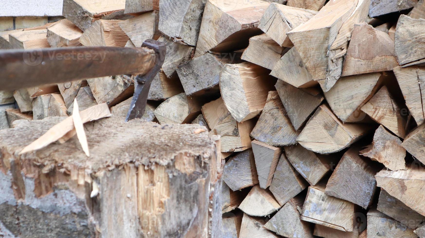 versnipperd brandhout voor de winter voor verwarming. de bijl wordt met een mes in de stronk gestoken. hakmes met een houten handvat. oogsten op de boerderij. droog brandhout gestapeld in stapels voor het verwarmen van een huis foto