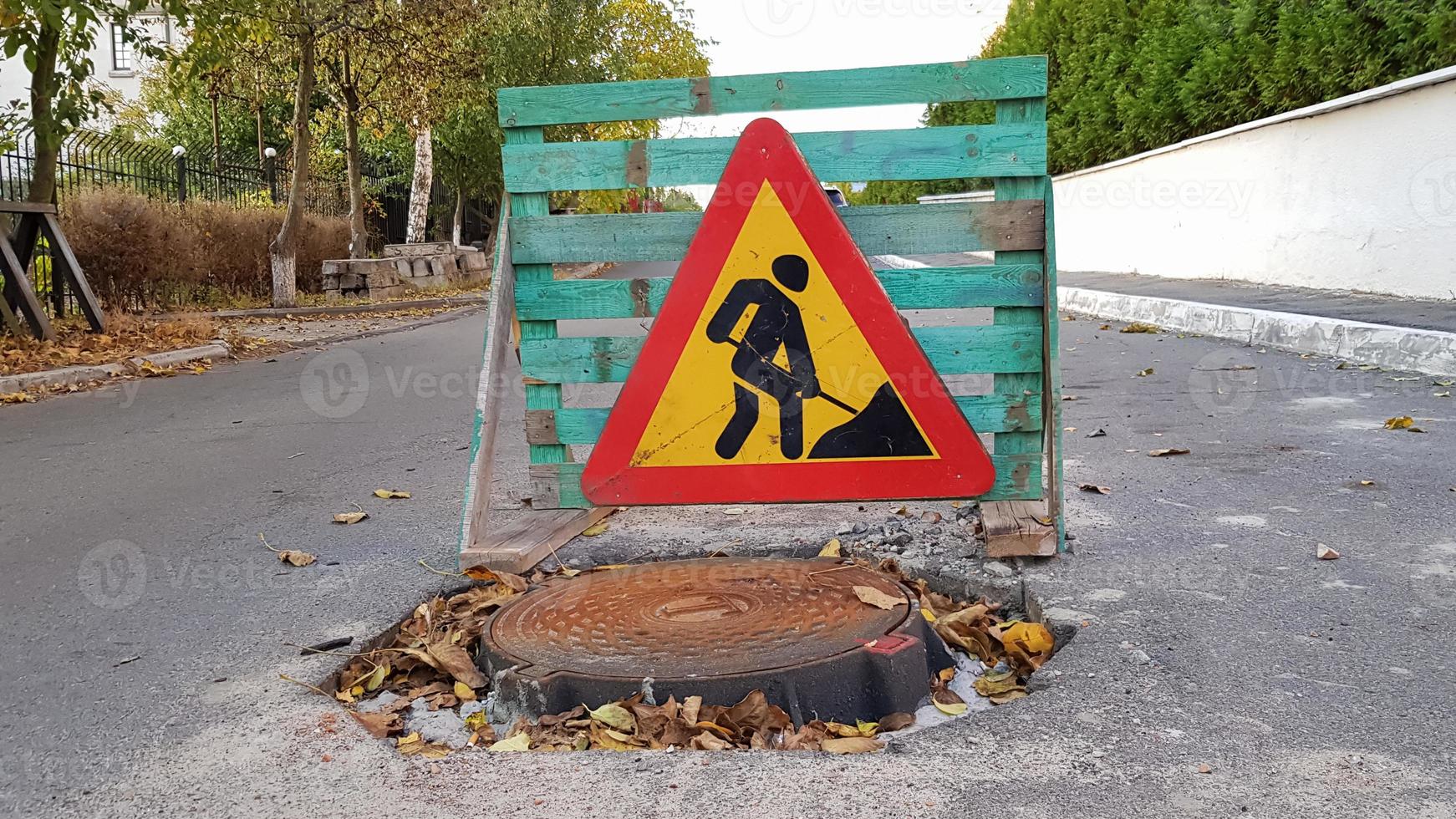 weg reparatie. riool mangat op de rijbaan. driehoekige waarschuwing automobilisten ondertekenen met een man met een gele schop met rood. mannen aan het werk. verkeersborden, reisbeperkingen. foto