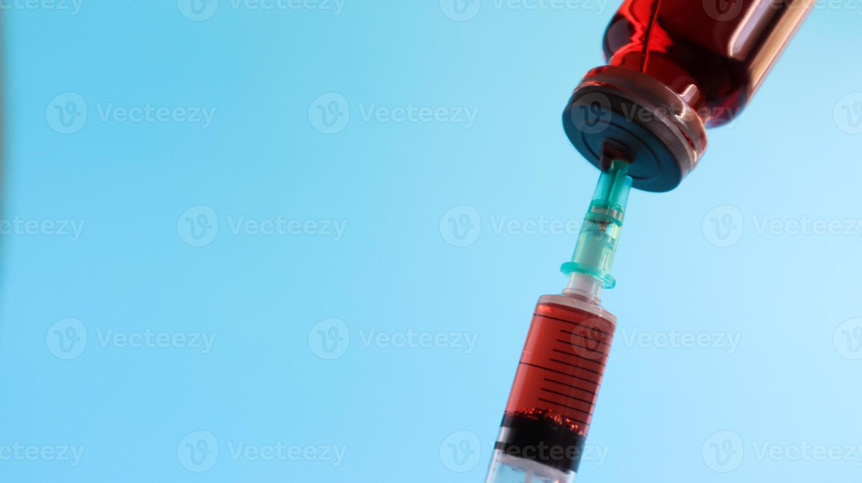 coronavirus griep en pandemische vaccins, spuit en injectieflacon met rode vloeistof op een blauwe achtergrond. medisch concept, onderhuidse injectie, behandeling van de ziekte. kopieer ruimte voor tekst of logo foto