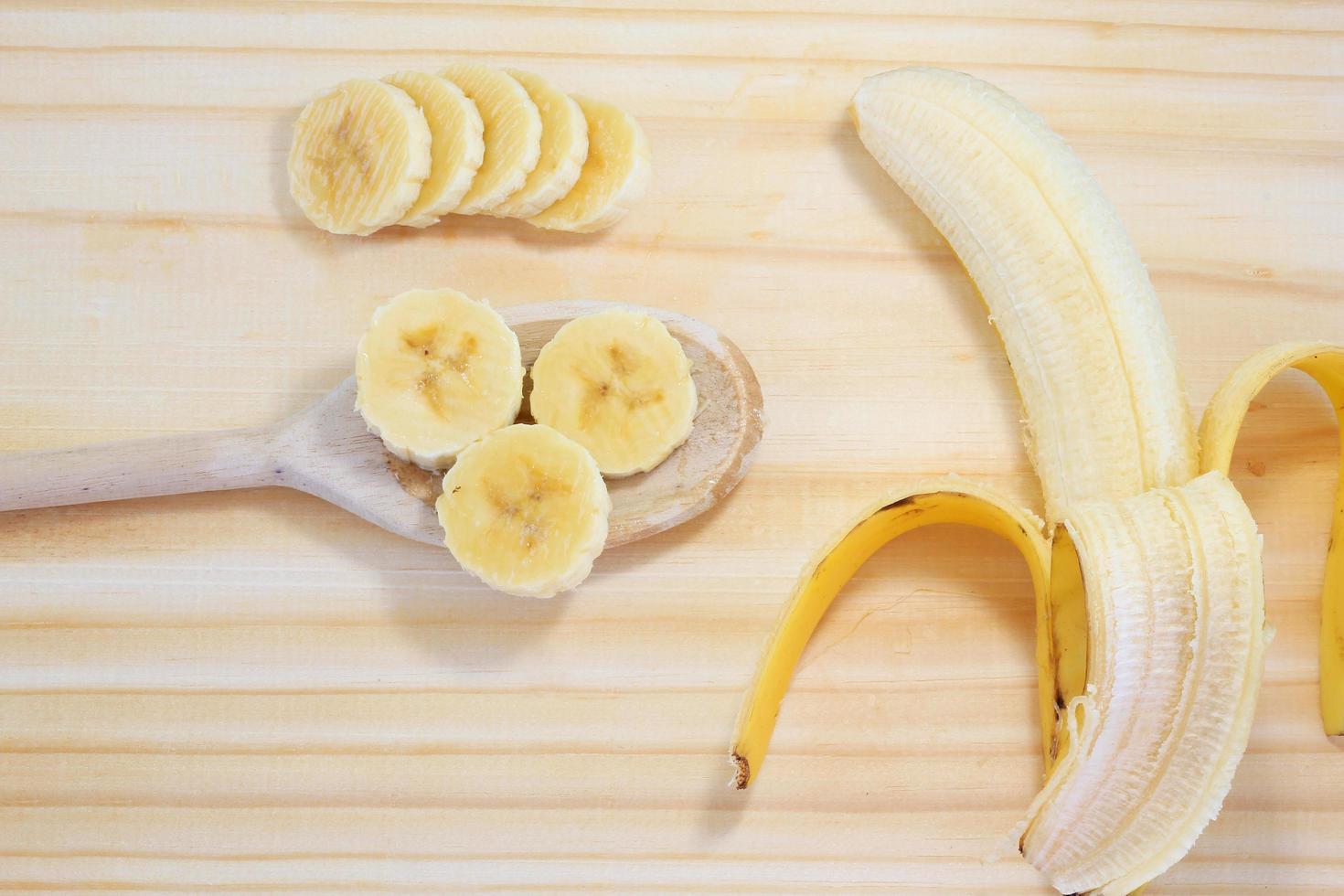 gepelde banaan op hout naast plakjes op houten lepel foto