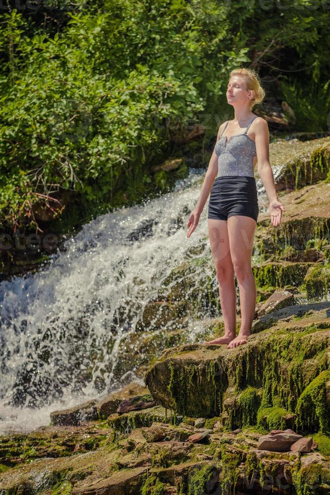 jonge vrouw die yogapositie doet dichtbij een waterval foto