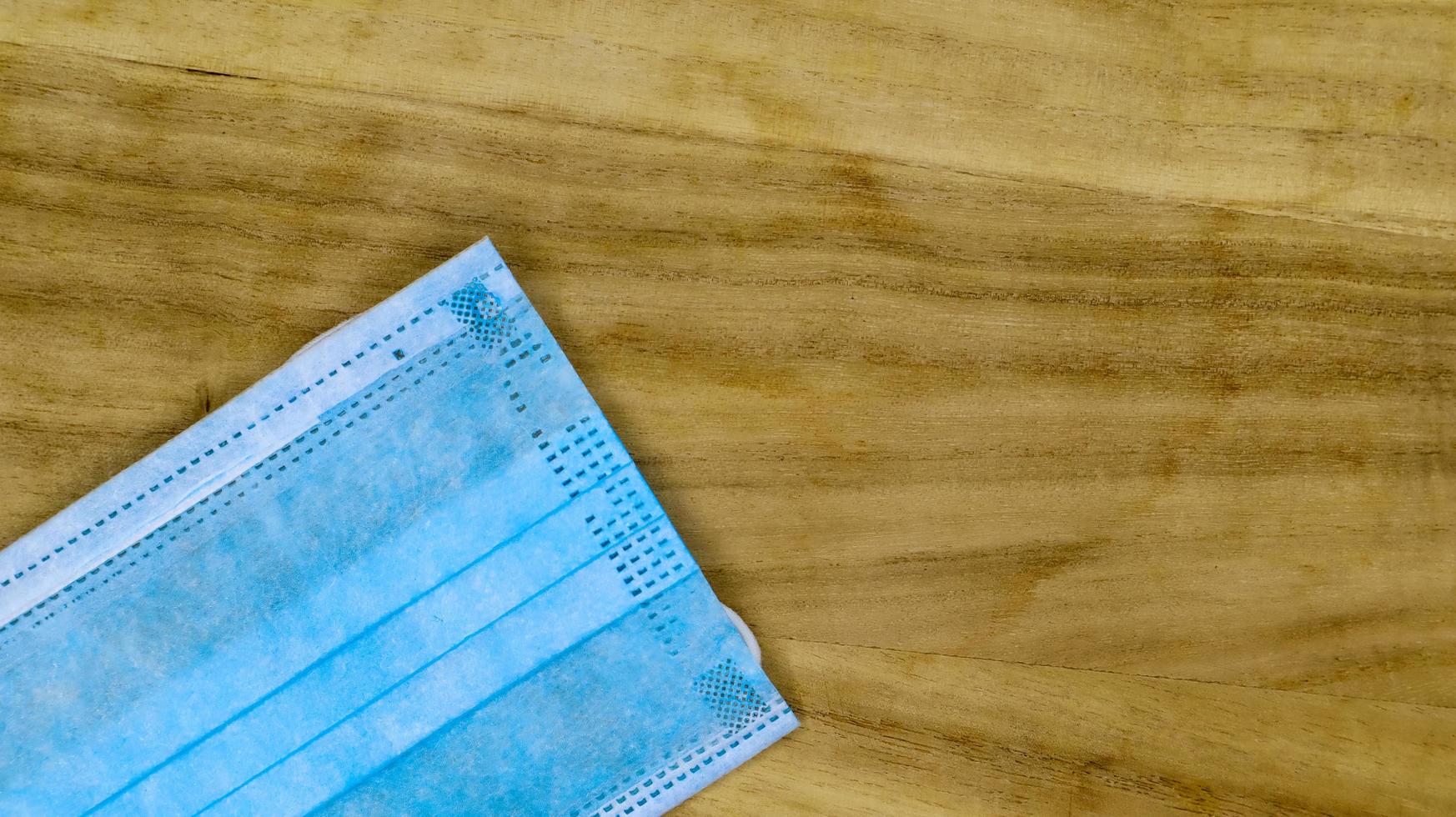 een 3-laags chirurgisch wegwerpmasker met rubberen kussentjes die de mond en neus bedekken op een houten tafel. het concept van bescherming tegen bacteriën, gezondheidszorg en medicijnen. covid19. gevaarlijk virus. foto