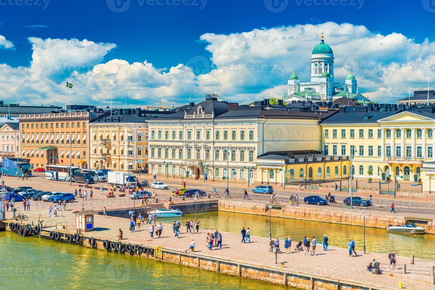 pittoresk stadsbeeld van helsinki, finland. uitzicht op het stadscentrum met historische gebouwen, de kathedraal, prachtige wolken in de blauwe lucht en mensen die langs een dijk lopen foto