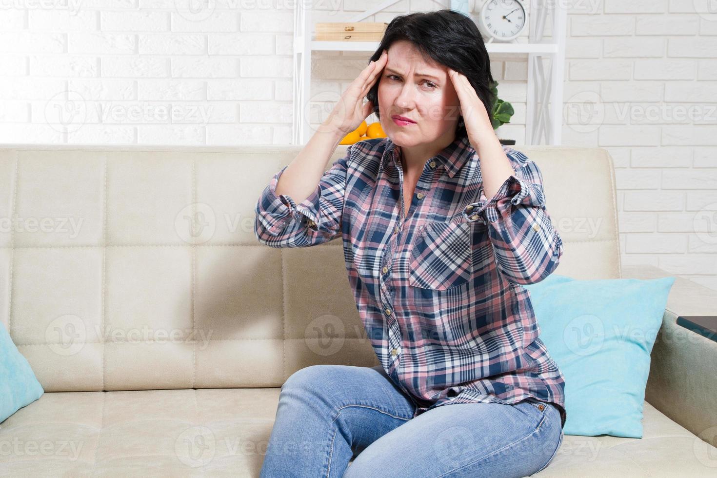 vrouw van middelbare leeftijd die lijdt aan stress of hoofdpijn, grijnzend van de pijn terwijl ze de achterkant van haar nek met haar andere hand tegen haar slaap houdt met kopieerruimte foto