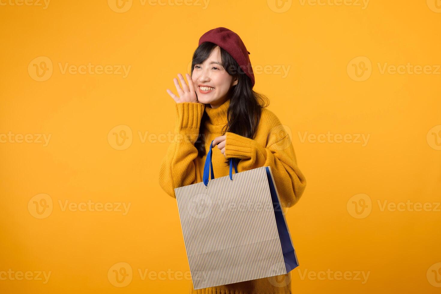 jong Aziatisch vrouw in haar jaren '30, vervelend een geel trui en rood baret, geniet korting boodschappen doen en geschreeuw naar vrij kopiëren ruimte tegen een levendig geel achtergrond. foto