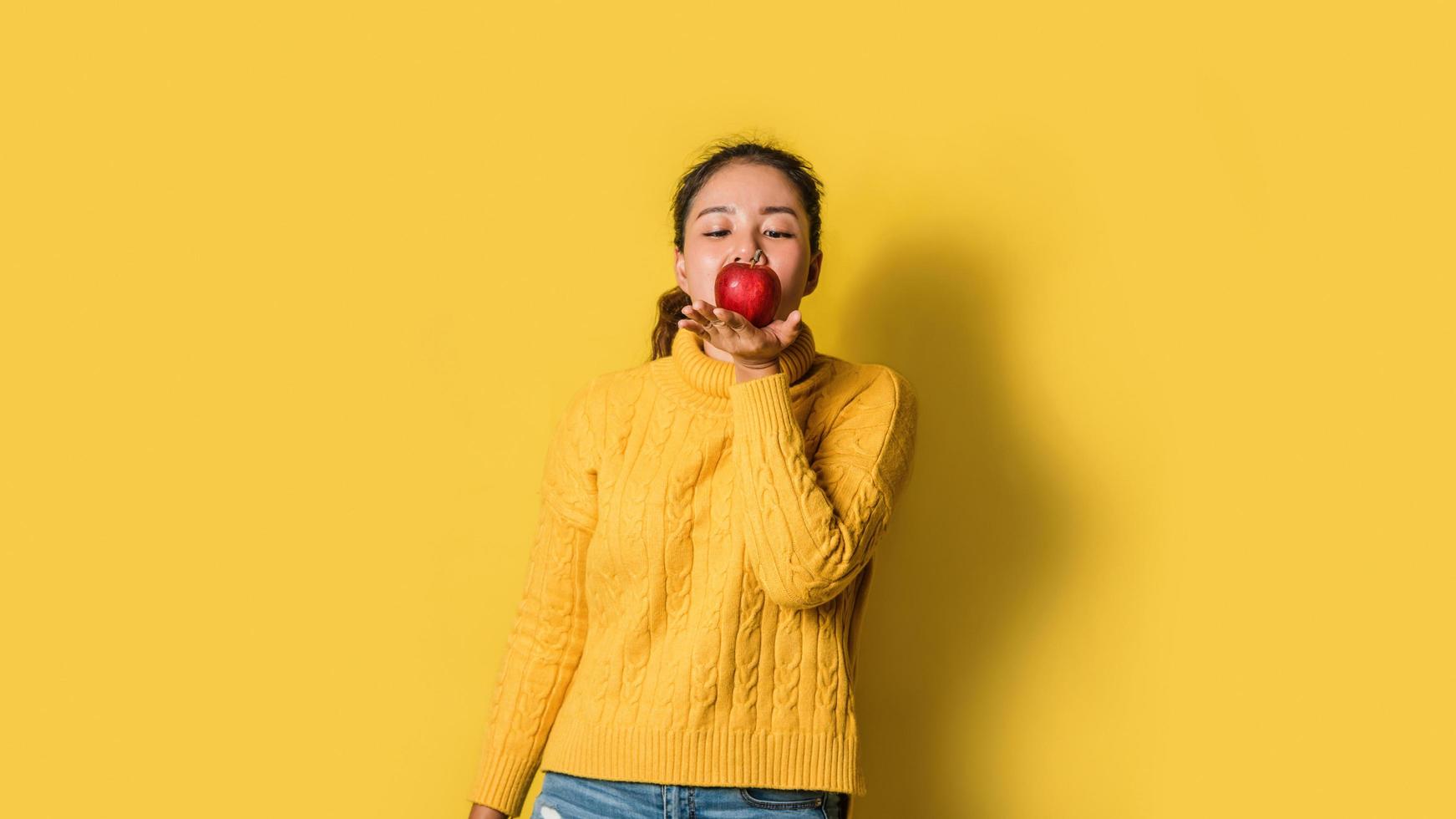 vrolijke jonge vrouw op gele achtergrond in studio met een rode appel in haar hand. het concept van lichaamsbeweging voor een goede gezondheid. gezondheidsliefhebber foto