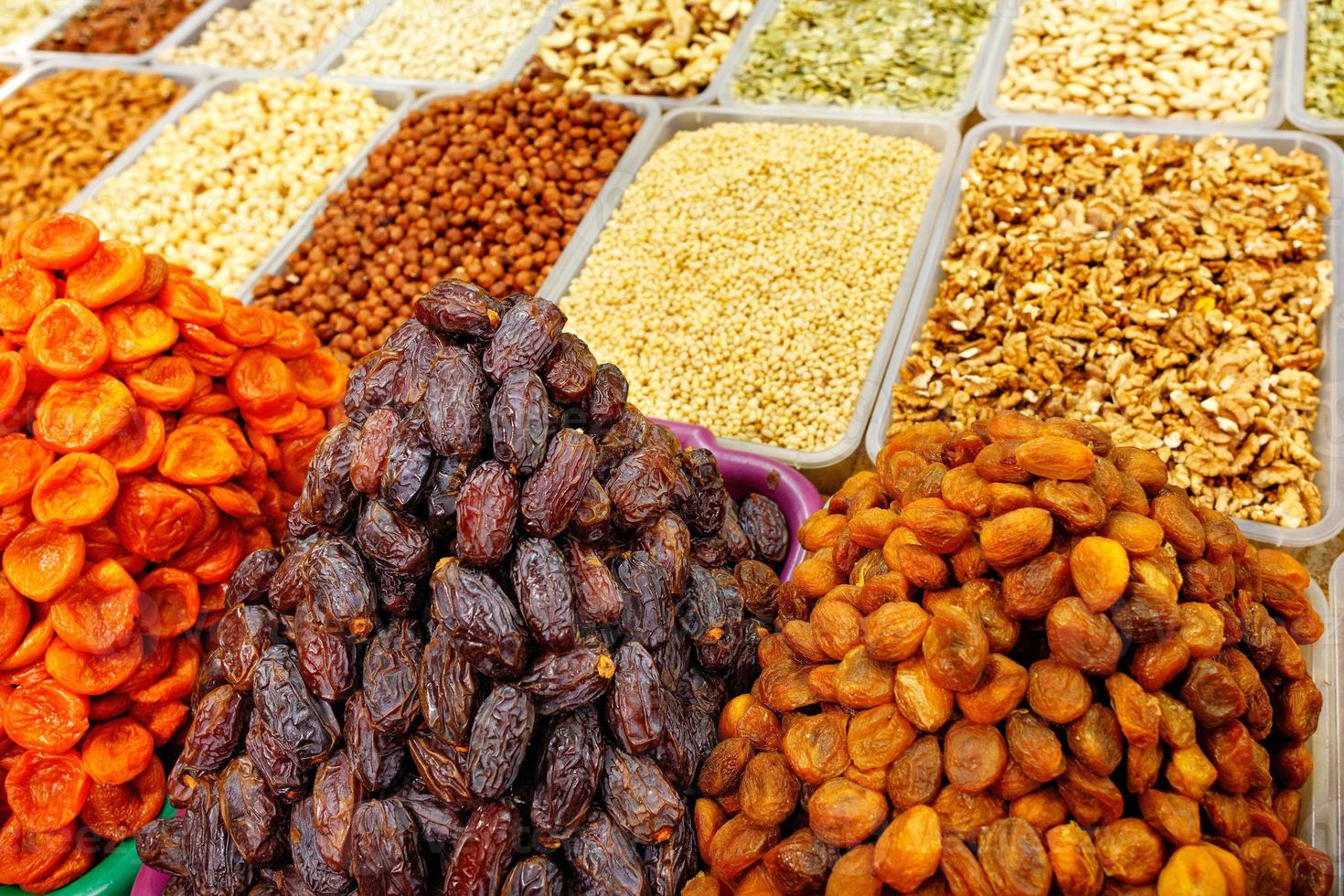dadels, gedroogde abrikozen worden op de markt verkocht op de achtergrond van verschillende noten, amandelen, hazelnoten, walnoten, cashewnoten in bewegingsonscherpte. foto