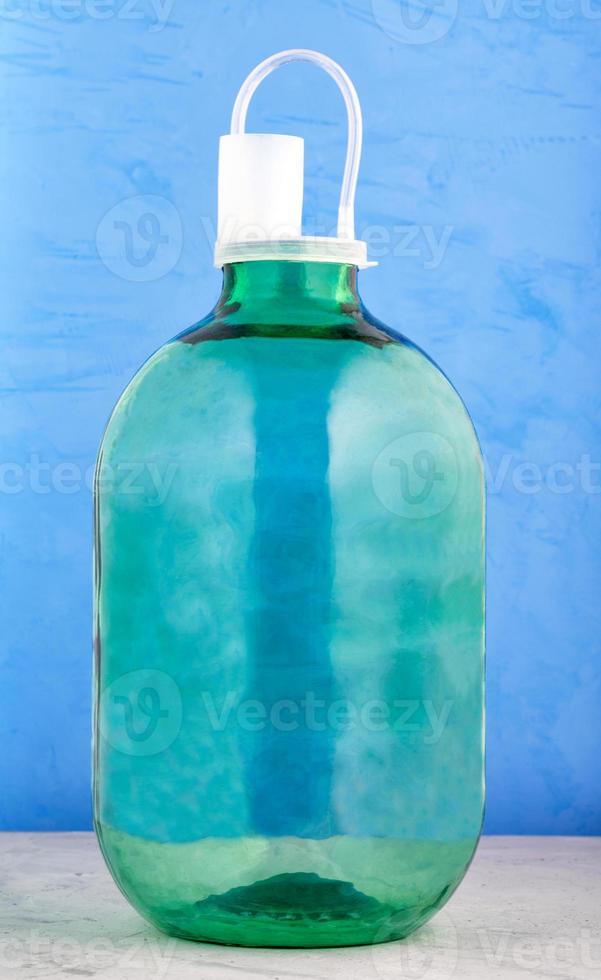 een glazen pot van 10 liter is gemaakt van dik groen glas met een nylon deksel met een waterslot op een blauwe achtergrond. foto