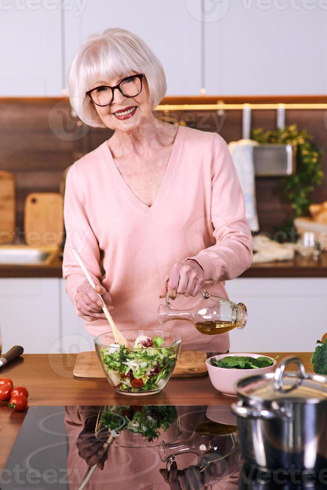 senior vrolijke vrouw kookt in de moderne keuken. voedsel, vaardigheden, levensstijlconcept foto