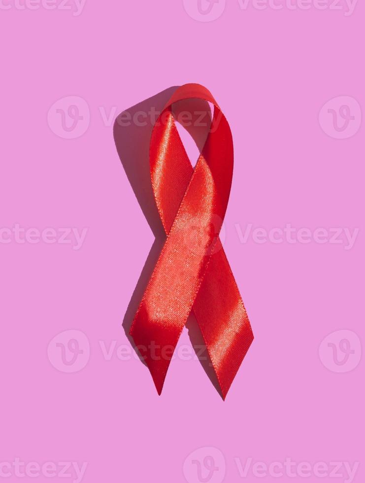 internationale aidsdag. rood lint met een harde schaduw op een roze achtergrond. helpt bewustzijn concept. verticaal foto