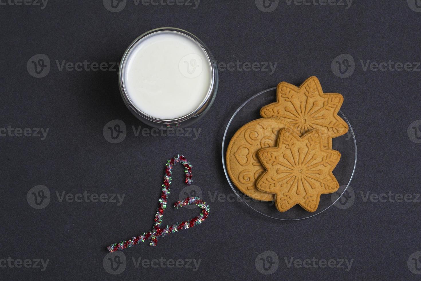 peperkoek en melk voor de kerstman. kerstcompositie met peperkoekkoekjes en melk op een zwarte achtergrond. foto