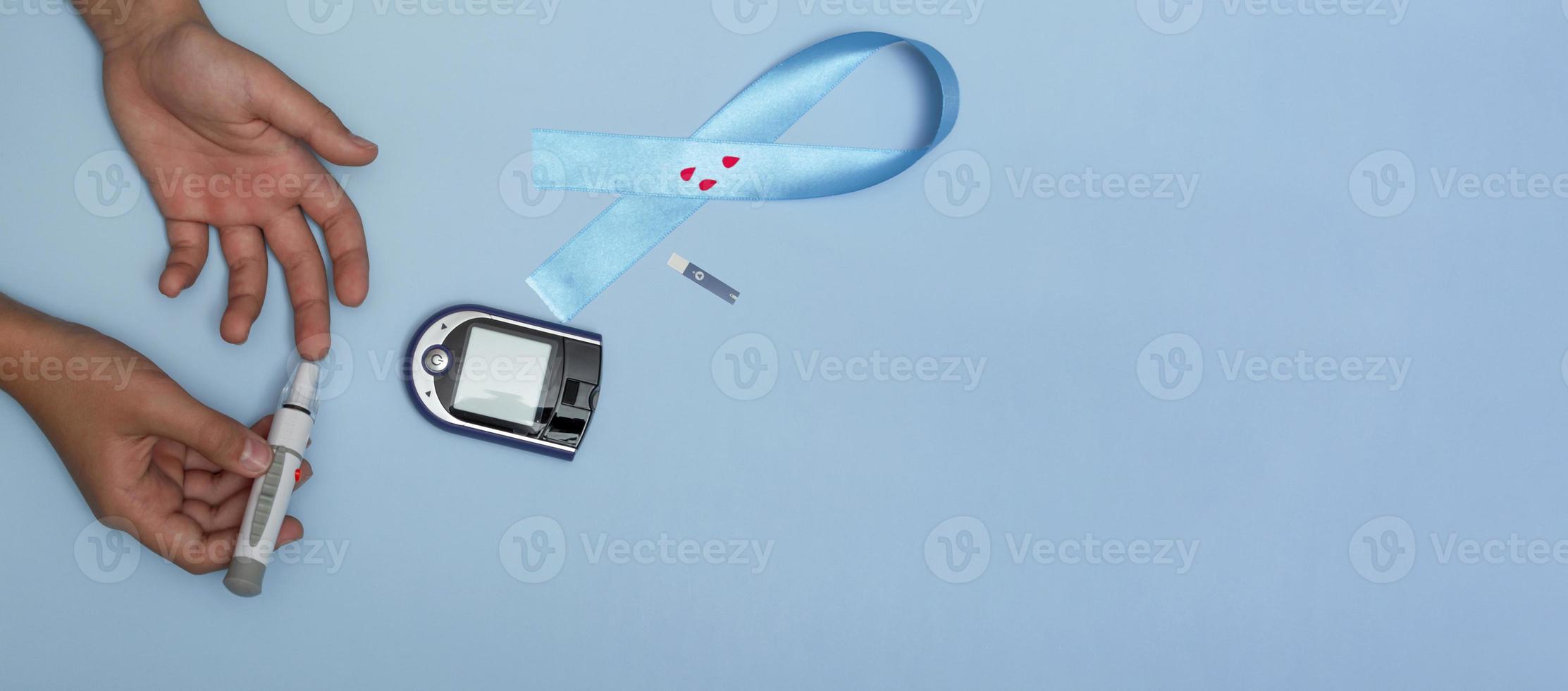 close-up bovenaanzicht van concept voor werelddiabetesdag 14 november. kind meet de bloedsuikerspiegel op een blauwe achtergrond en een blauw lint met bloeddruppels foto