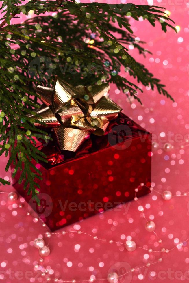 een fantastisch cadeau in een rode doos met een gouden lint onder de kerstboom, op een roze achtergrond met bokeh. nieuwjaar en kerst. foto