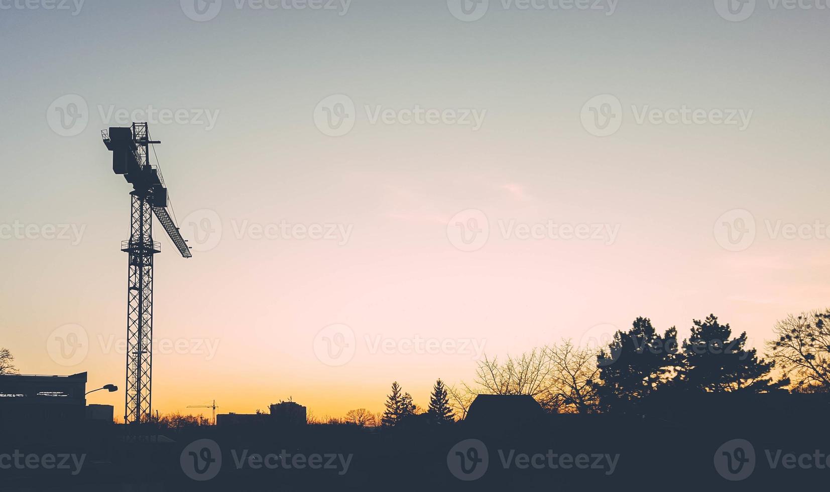 silhouet van een bouwtorenkraan tegen de achtergrond van de avondstad en een prachtige zonsondergang. horizon tussen lucht en huizen. foto