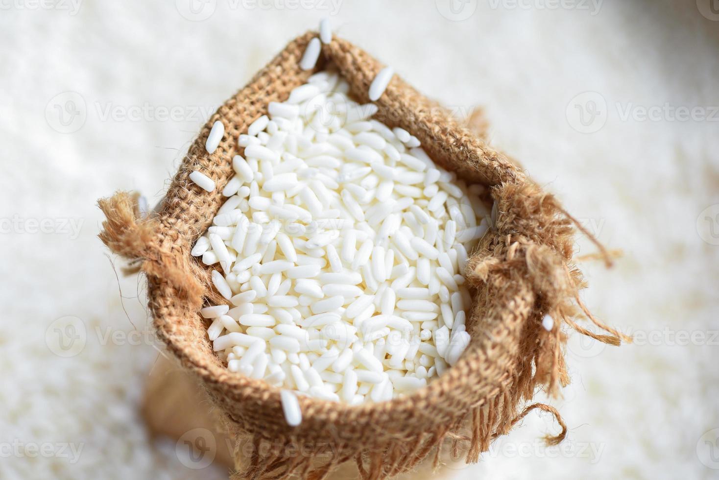 jasmijn witte rijst in zak en geoogste rijst op houten tafel, oogst rijst en voedselkorrels kookconcept foto