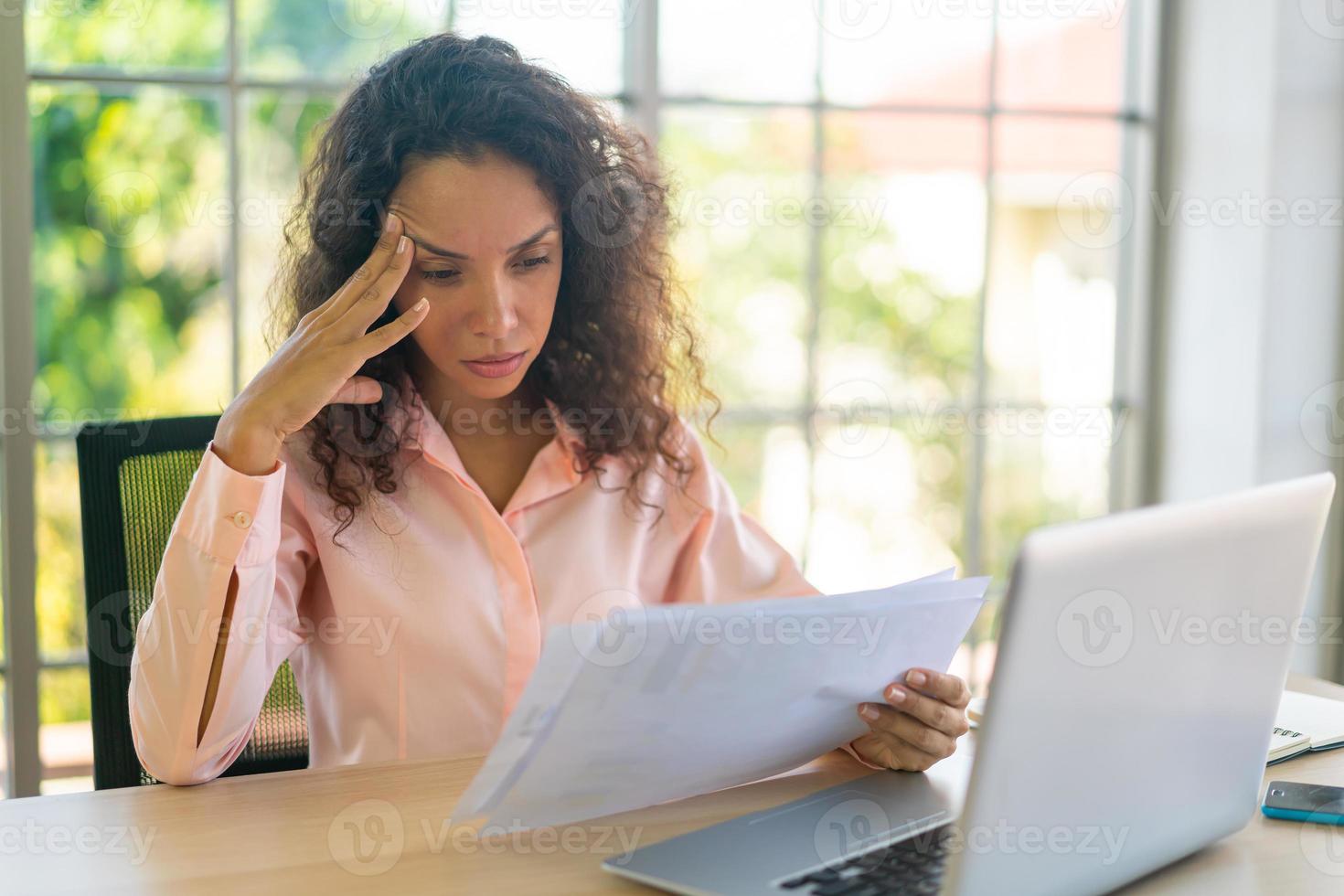 Latijnse vrouw die met laptop en papier op werkruimte werkt foto