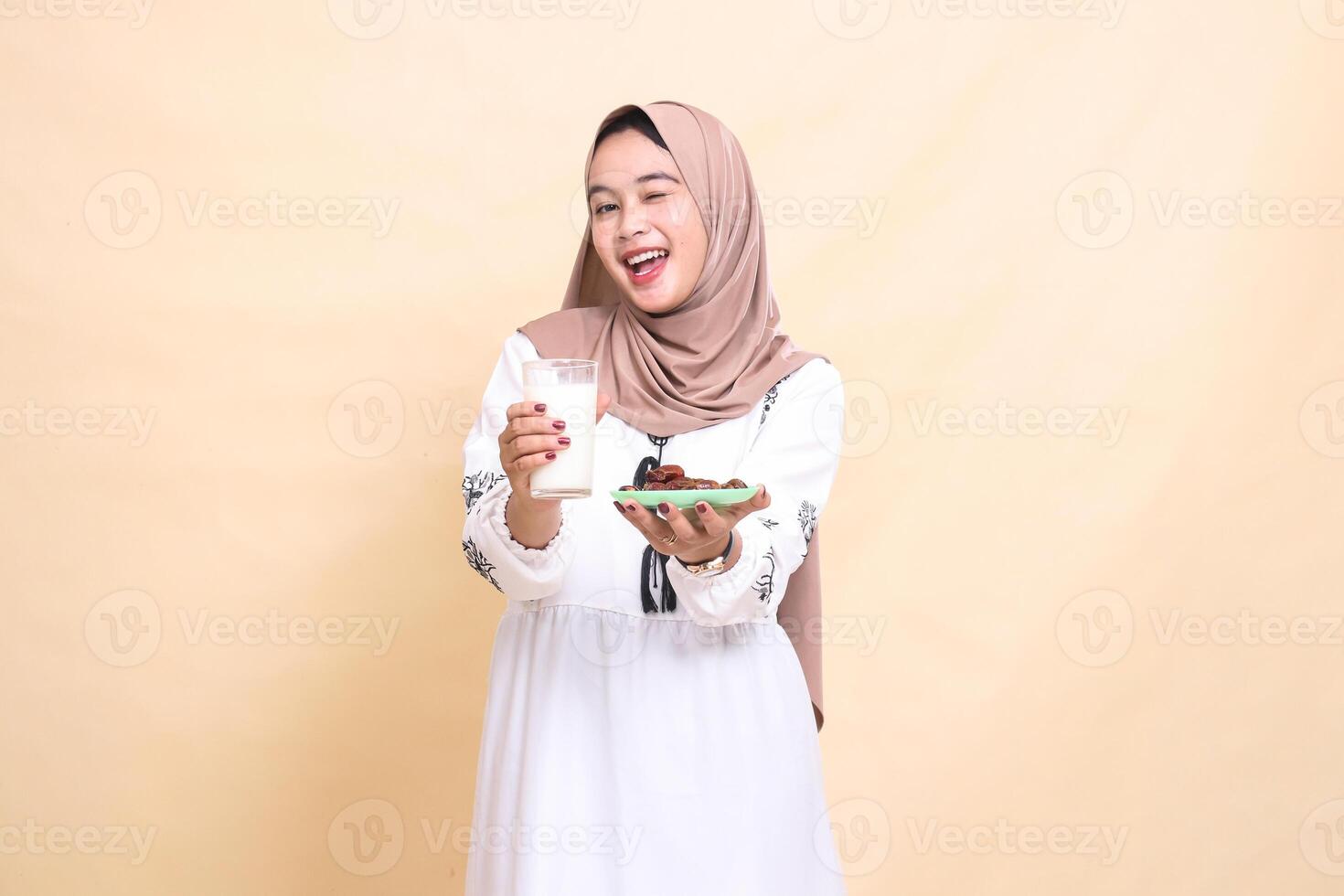 een mooi Indonesië moslim meisje vervelend een hijab glimlacht vrolijk en knipoogt, brengen een glas van melk en datums naar de voorkant terwijl breken de snel. gebruikt voor reclame, Gezondheid, eid en Ramadan foto