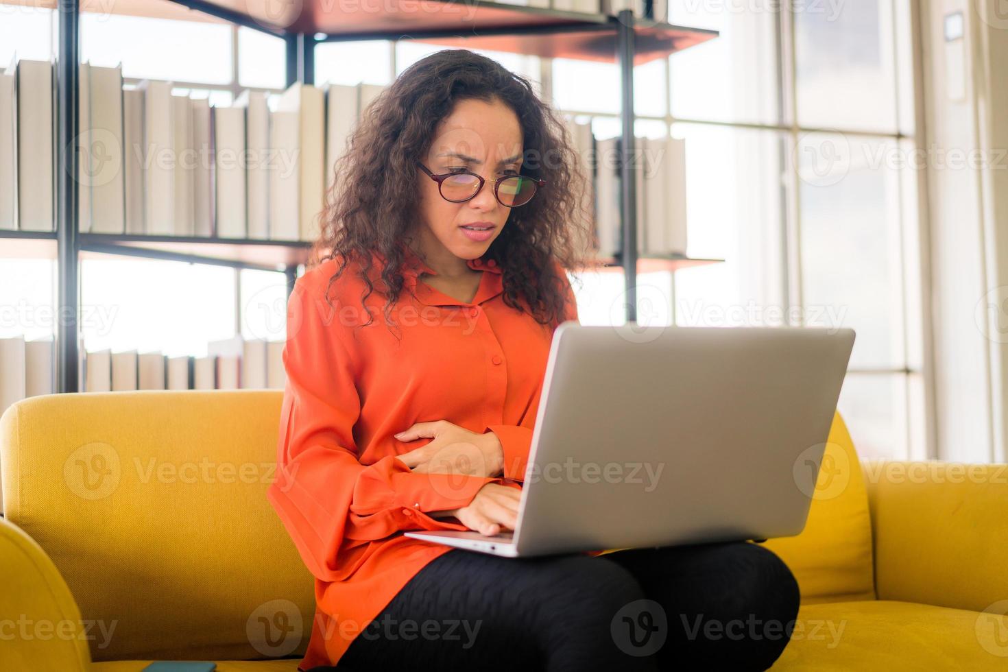 Latijnse vrouw die met laptop op bank met vermoeid gevoel werkt foto