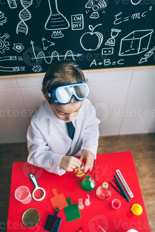 kind speelt met chemische vloeistoffen boven tafel foto