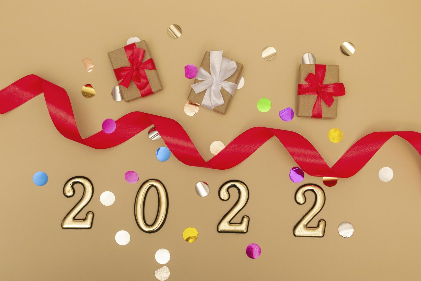 nieuwjaar 2022. bovenaanzicht nieuwjaarsmodel op beige achtergrond rood lint, geschenkdoos, gouden cijfers en veelkleurige sparkles. lay-out van ansichtkaarten, uitnodigingen. foto