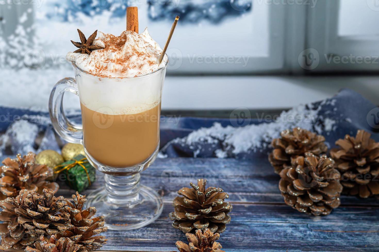 hete koffie latte met kaneelstokjes, bestrooid met kaneel. kerstversiering, takken van een kerstboom. vakantie concept nieuwjaar. foto