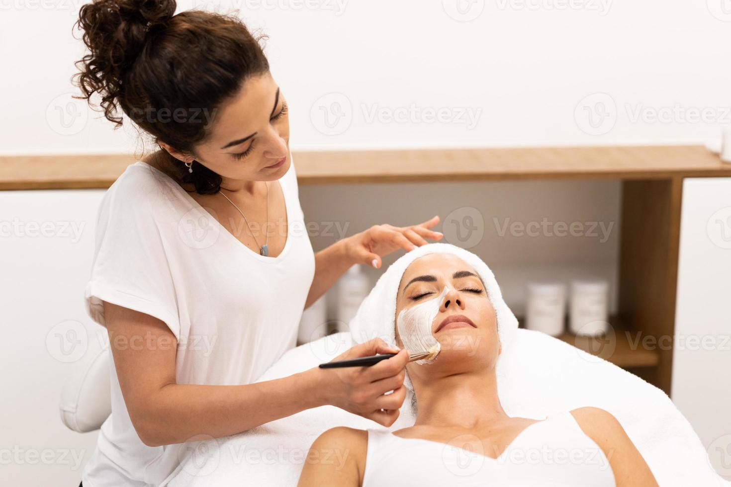 esthetiek die een masker toepast op het gezicht van een vrouw van middelbare leeftijd in een modern wellnesscentrum. foto