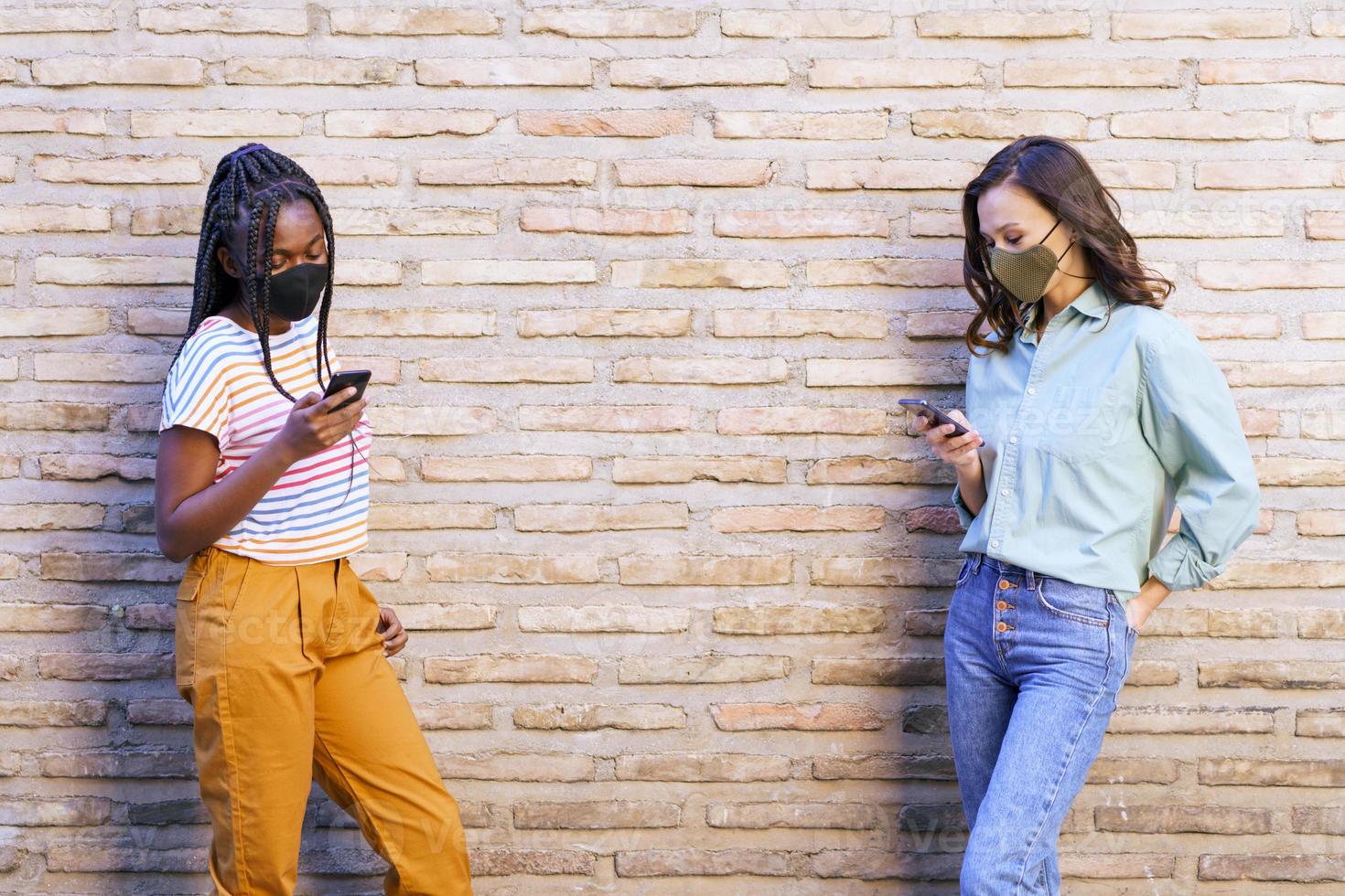 multi-etnische jonge vrouwen die maskers dragen die smartphone gebruiken gescheiden om sociale afstand te respecteren. foto