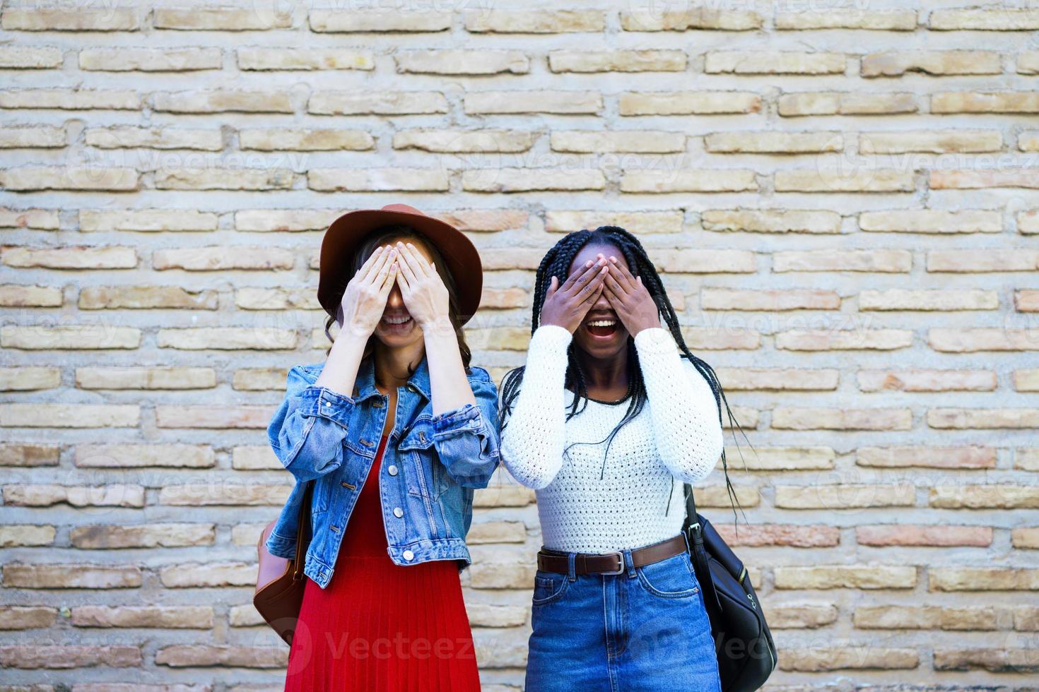 twee vrouwelijke vrienden die hun ogen buitenshuis bedekken. multi-etnische vrouwen. foto