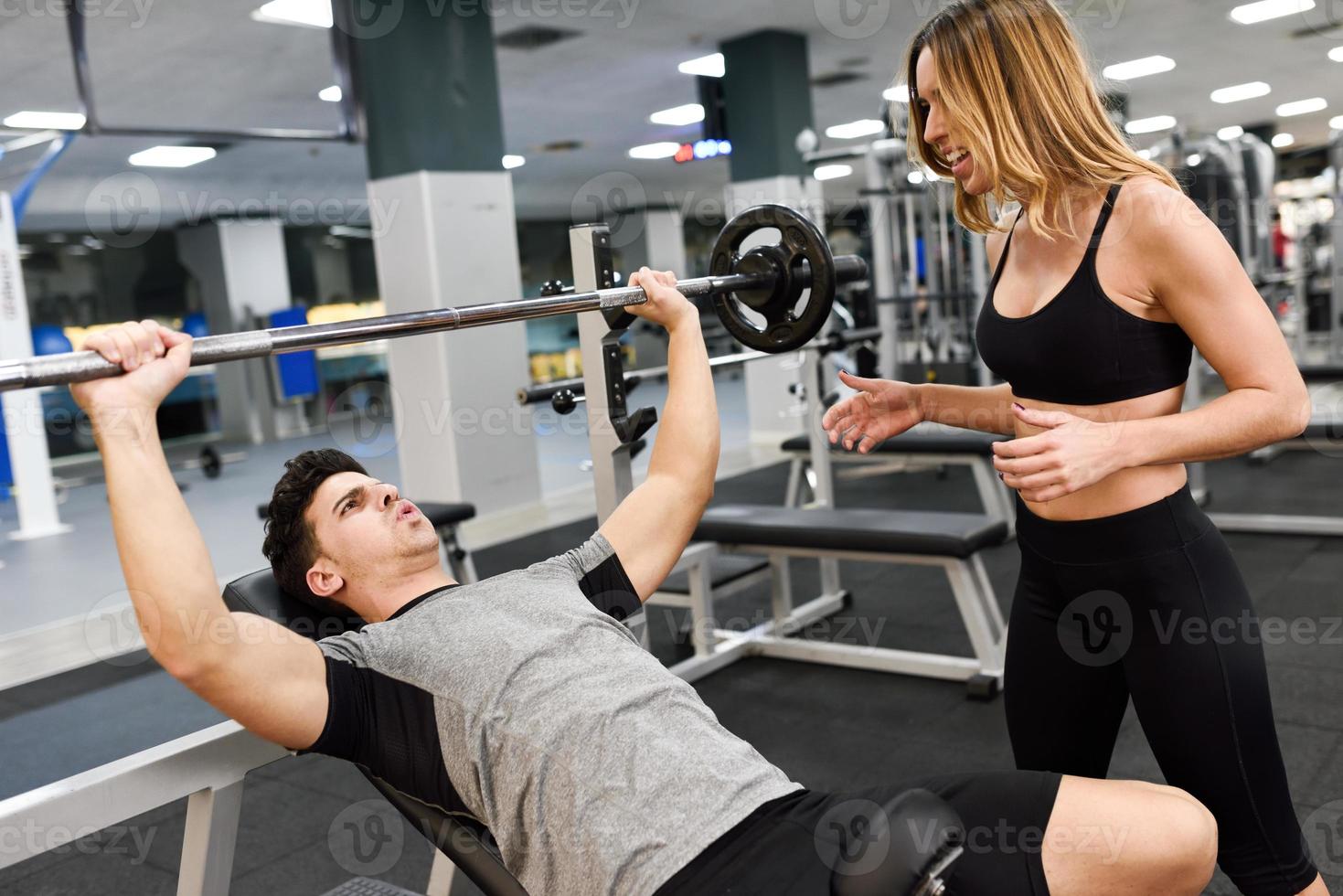 vrouwelijke personal trainer die een jonge man motiveert om gewichten op te heffen foto