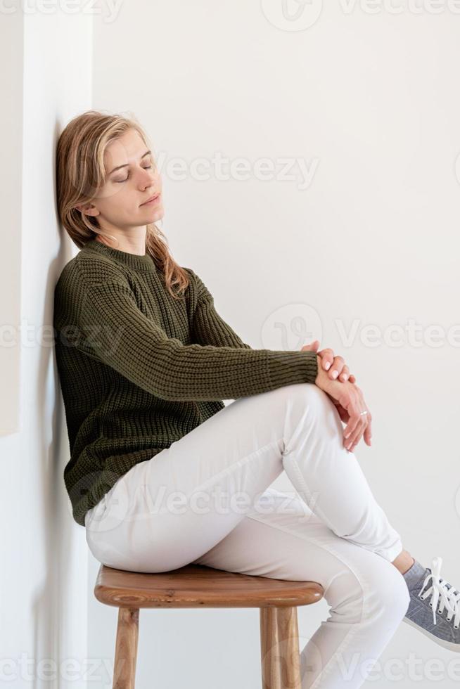 aantrekkelijke jonge vrouw zittend op de stoel in een licht en luchtig interieur met gesloten ogen foto