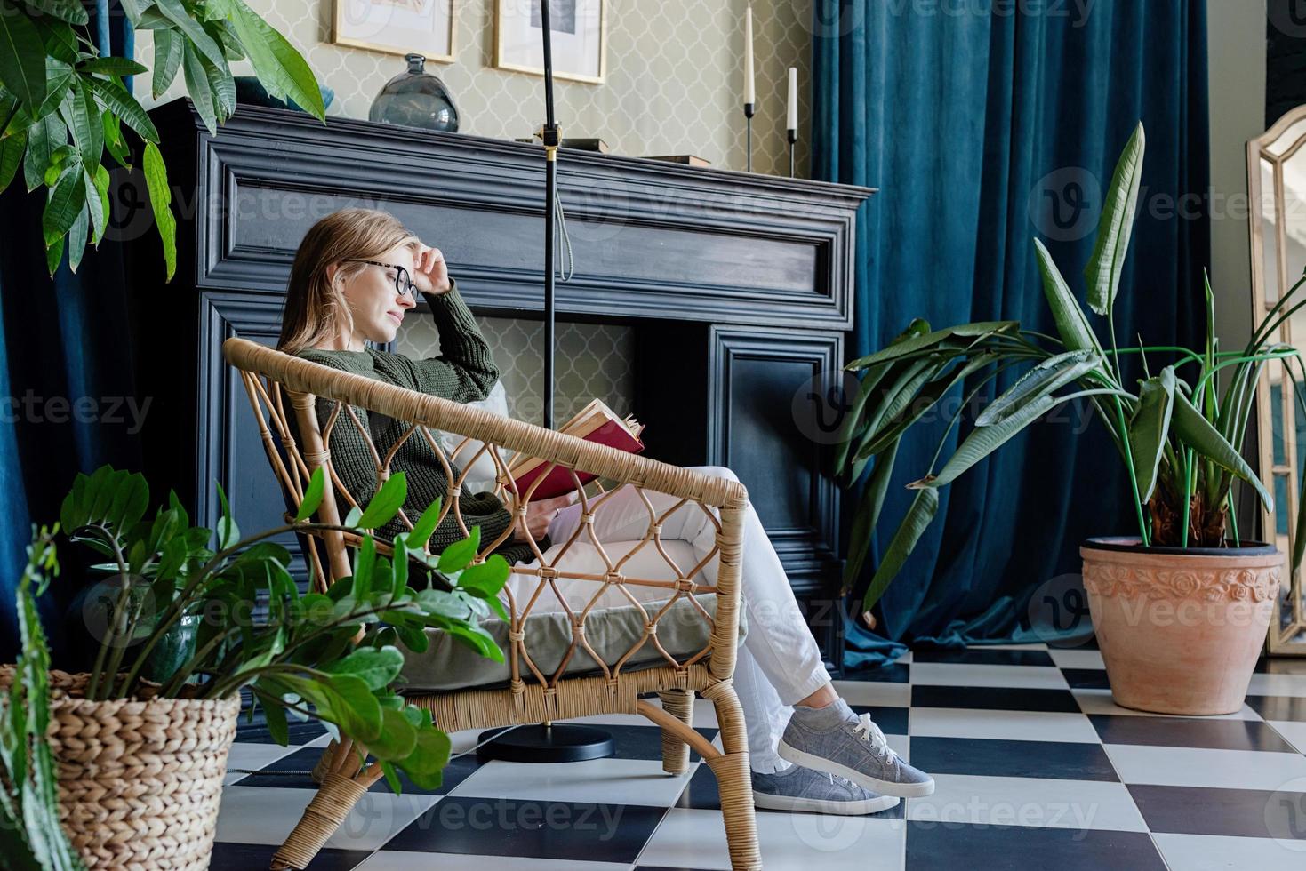 jonge blonde vrouw zit in een comfortabele stoel en leest een boek foto