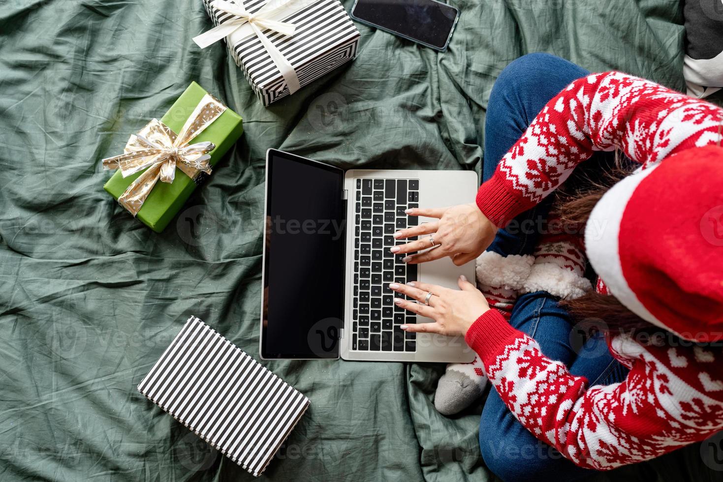 vrouw die kerstkleren draagt en op het bed zit met een laptop foto