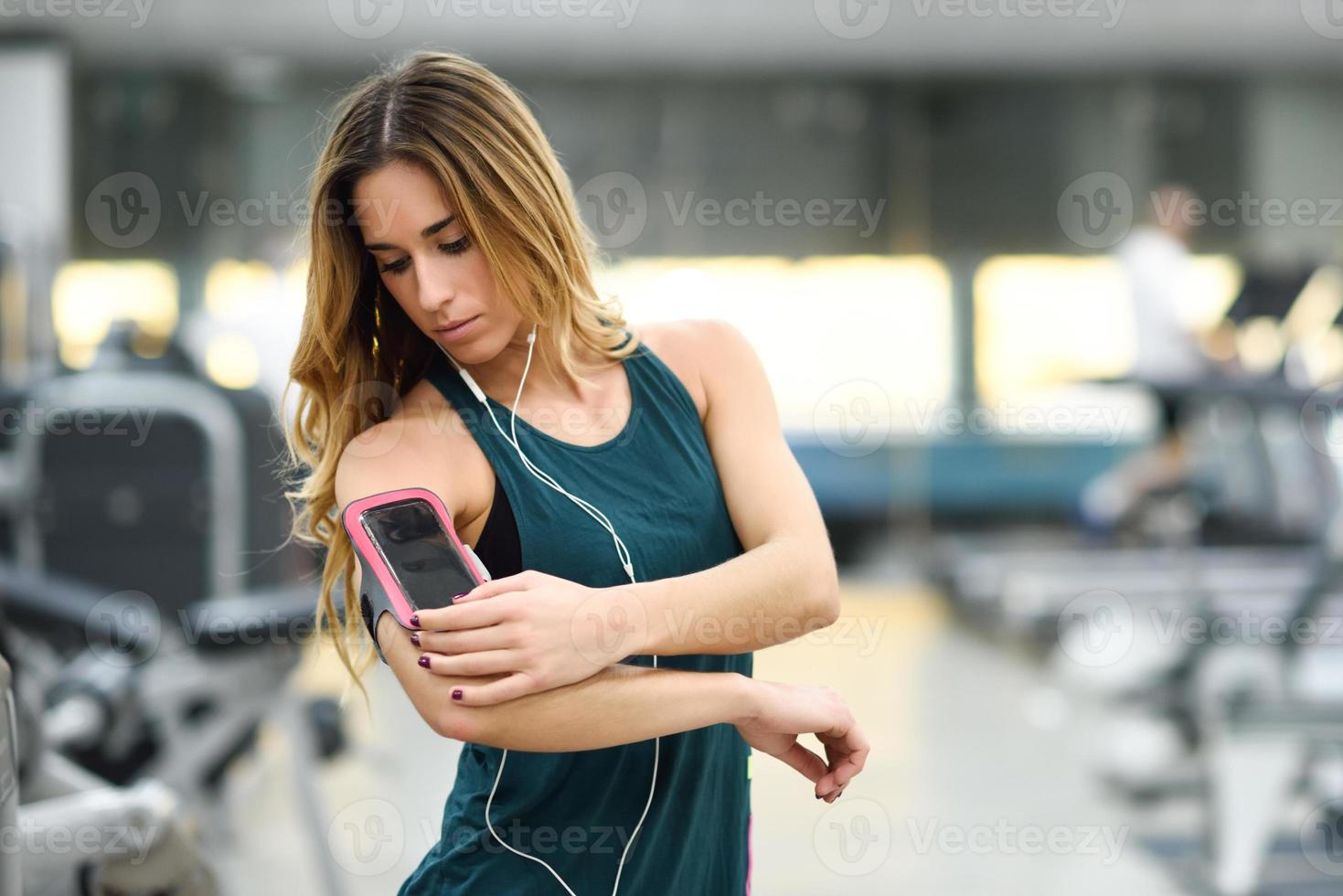 jonge vrouw die smartphone gebruikt die in de sportschool staat foto