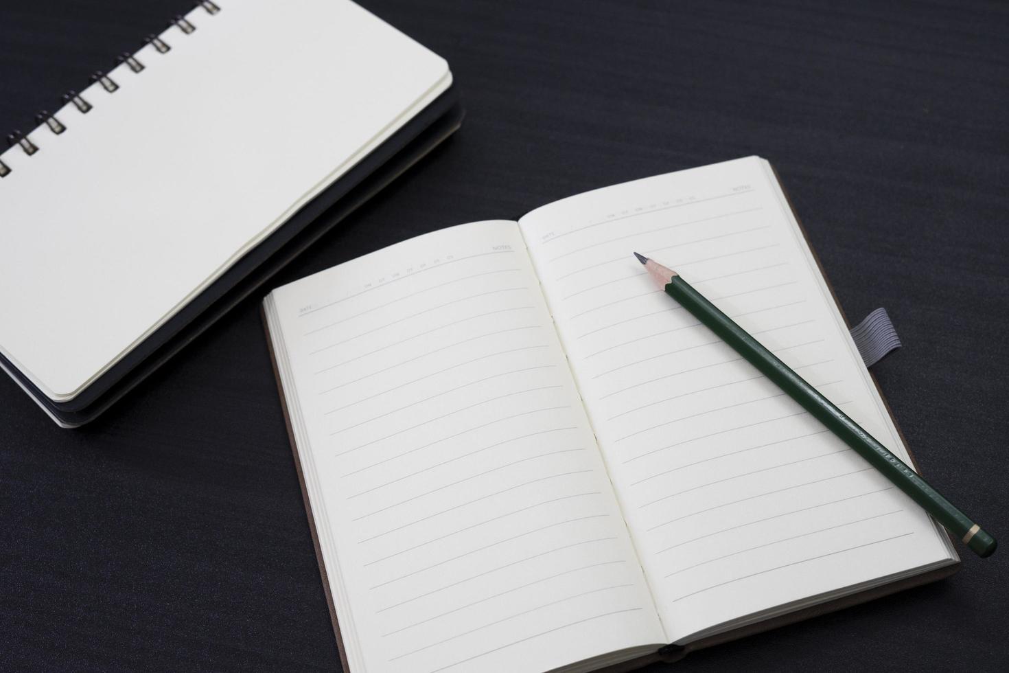 zwart bureau met notitieboekje en potlood erop. een notebookmodel op het bureau als indeling van de werkruimte. office-object geïsoleerd op zwarte achtergrond. foto