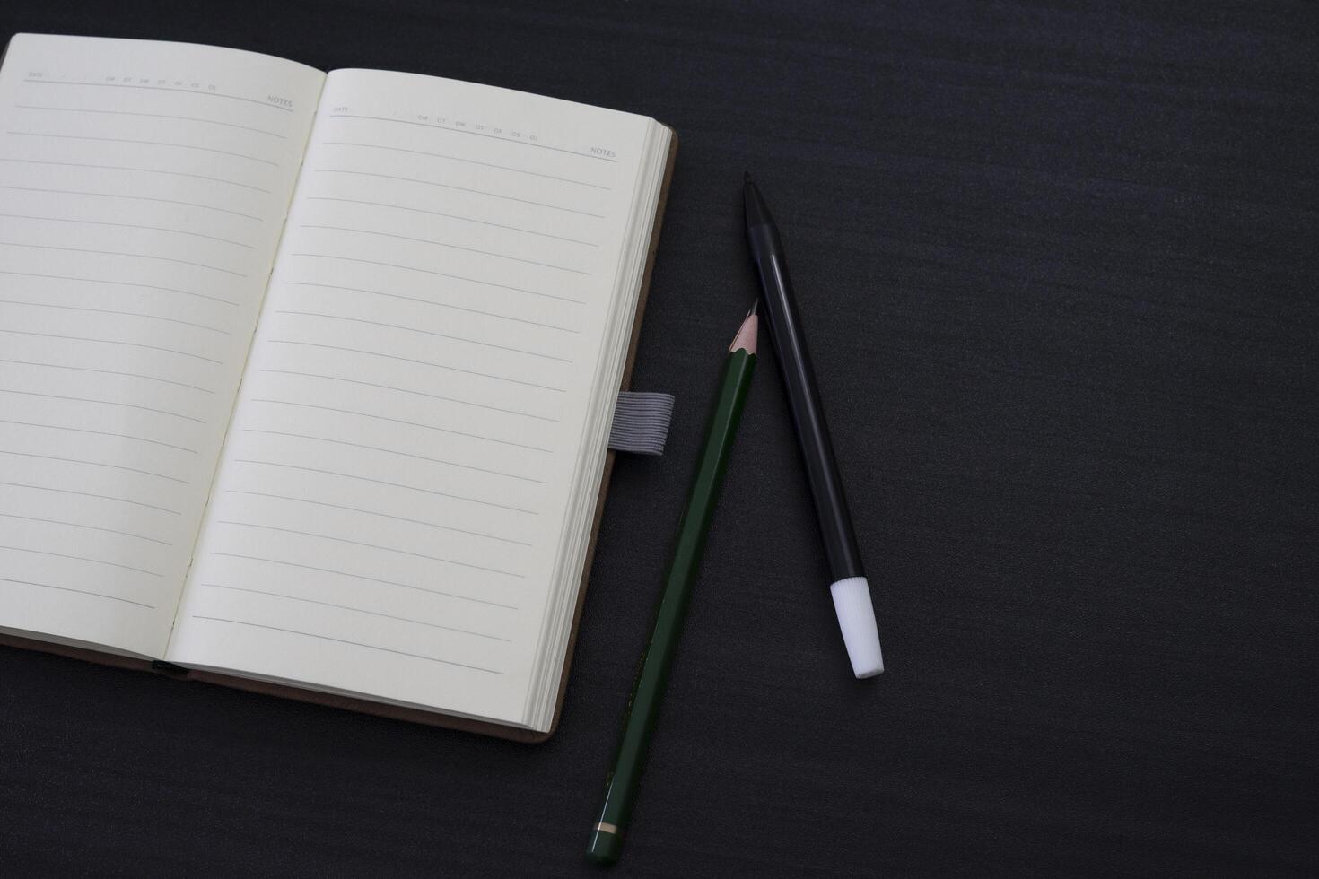 zwart bureau met notitieboekje en potlood erop. een notebookmodel op het bureau als indeling van de werkruimte. office-object geïsoleerd op zwarte achtergrond. foto