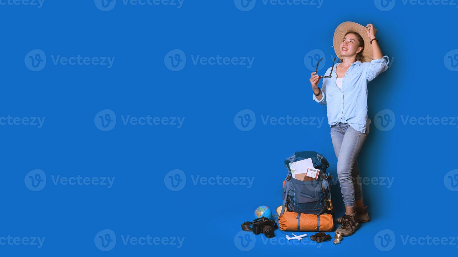 jonge Aziatische reiziger gelukkige vrouw in blauw shirt met rugzak met en uitrusting voor reizigers vakantie met een kaart, op blauwe kleur achtergrond. reis rugzak foto