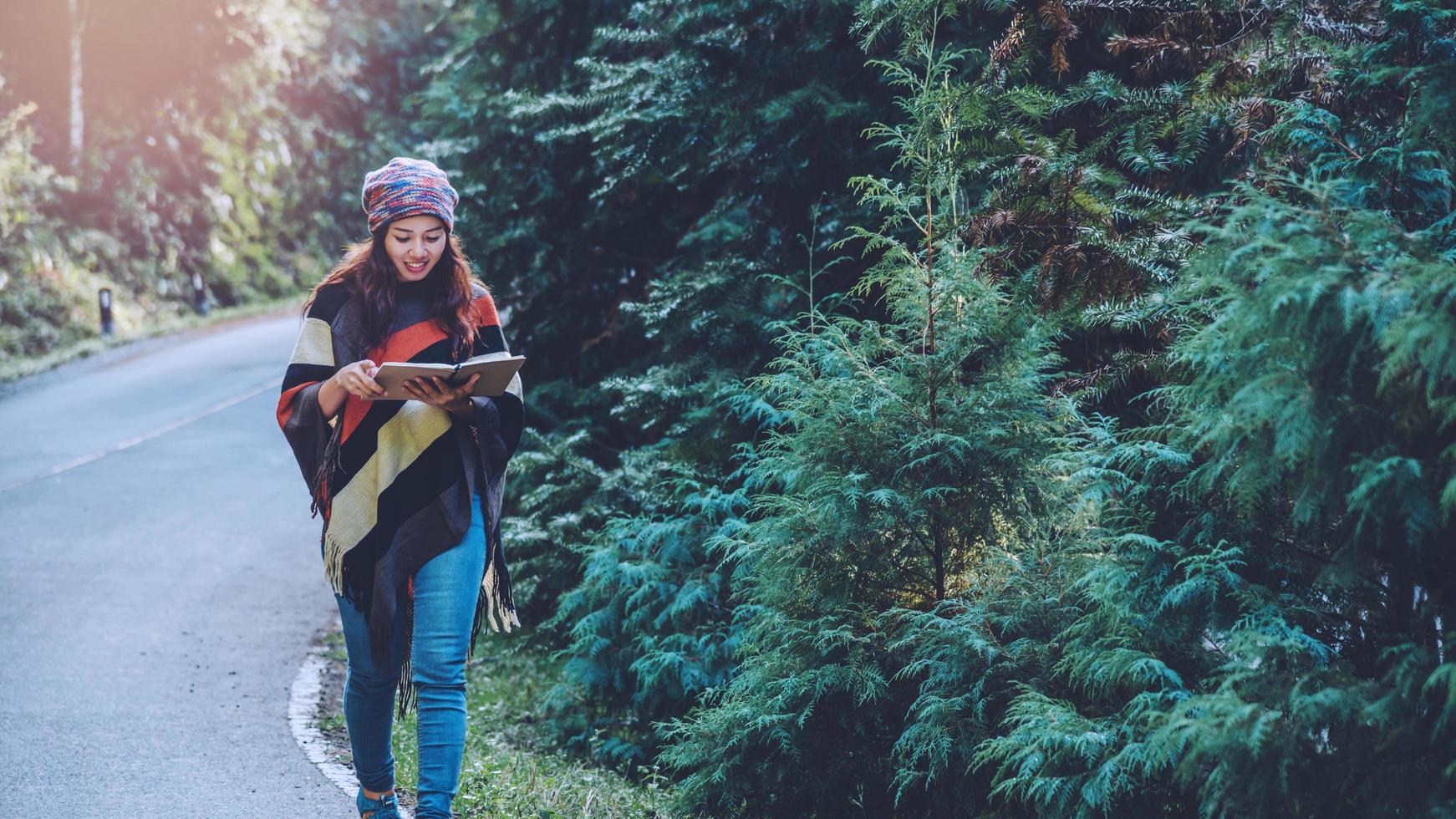 jonge vrouw reizen natuur. ze loopt op asfaltweg in bos dennengroen en schrijft een briefje tussen de pijnbomen genietend van de natuur. foto