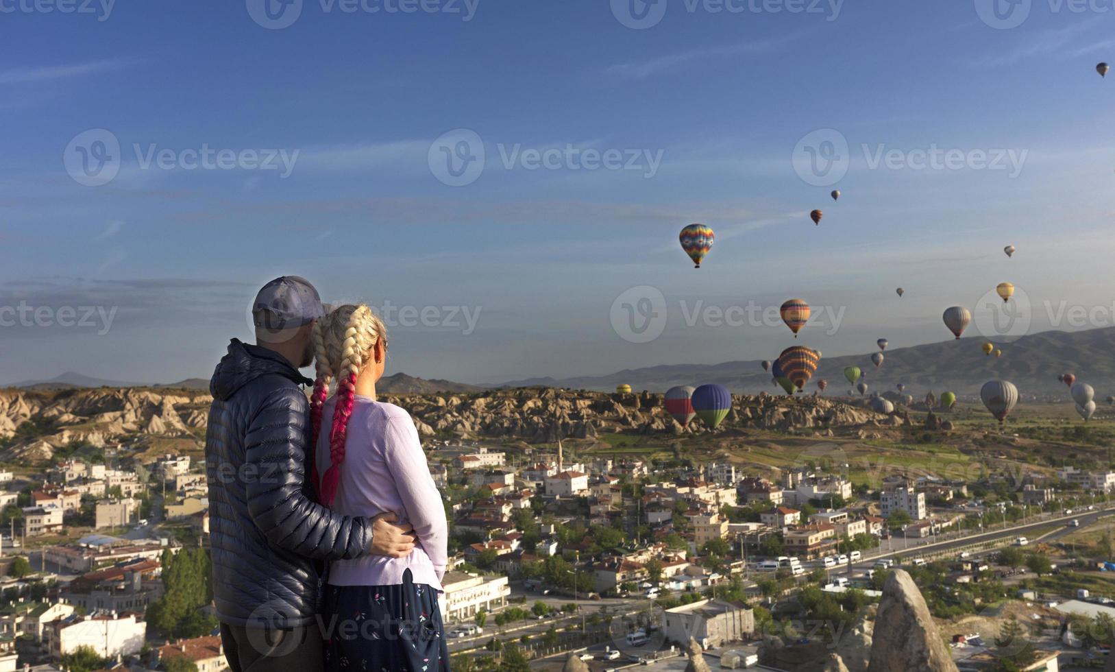 een jong stel kijkt toe hoe tientallen ballonnen over de valleien in Cappadocië vliegen. foto