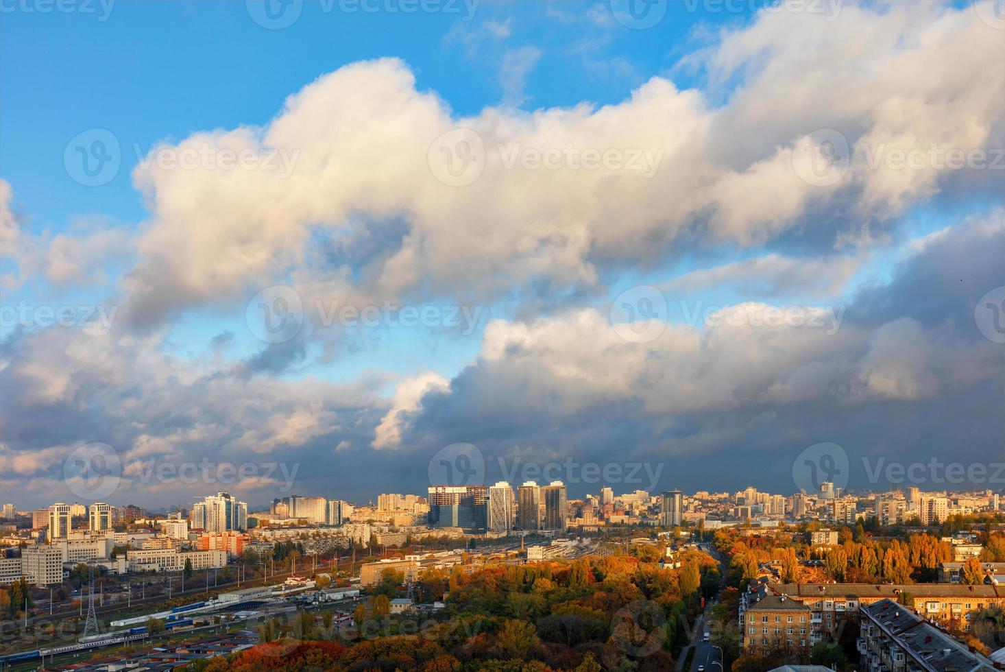 het kleurrijke stadsbeeld van de herfst Kiev, de zonnestralen van achter grijze wolken vangen en verlichten het oranje gebladerte van het stadspark. foto