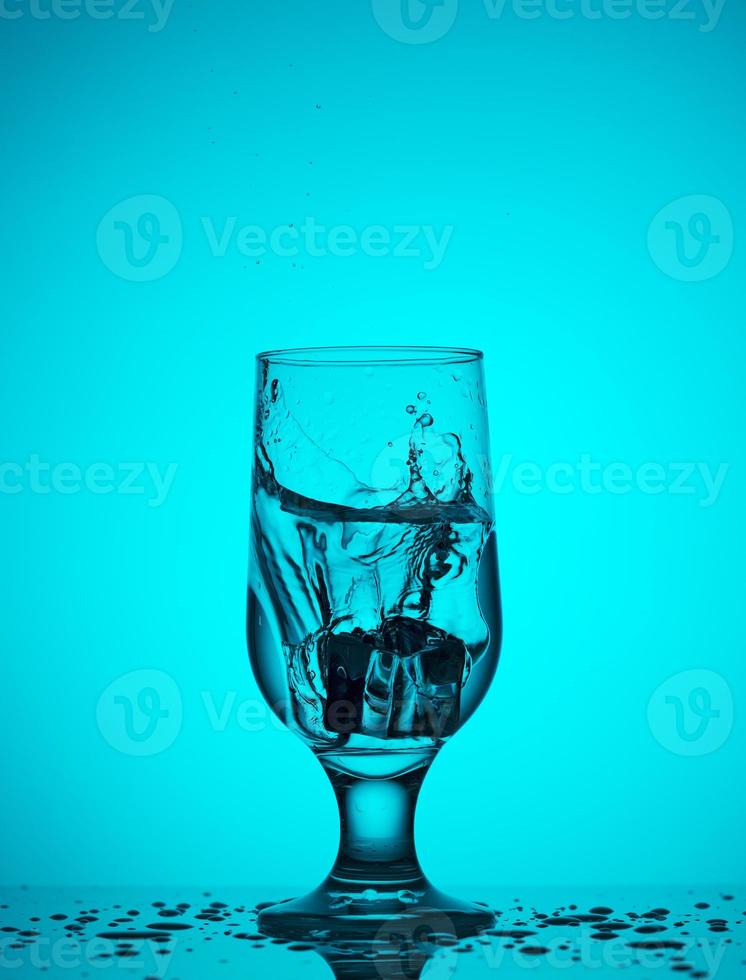 een ijsblokje valt in een glas met water foto