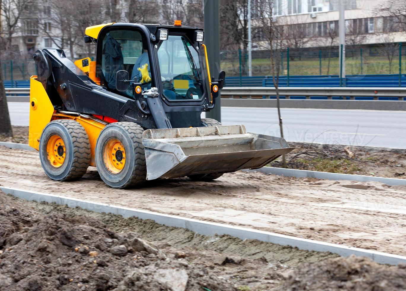 kleine behendige weggrader in beweging op een stoep in aanbouw in een lichte vervaging tegen de achtergrond van een stadsweg. foto