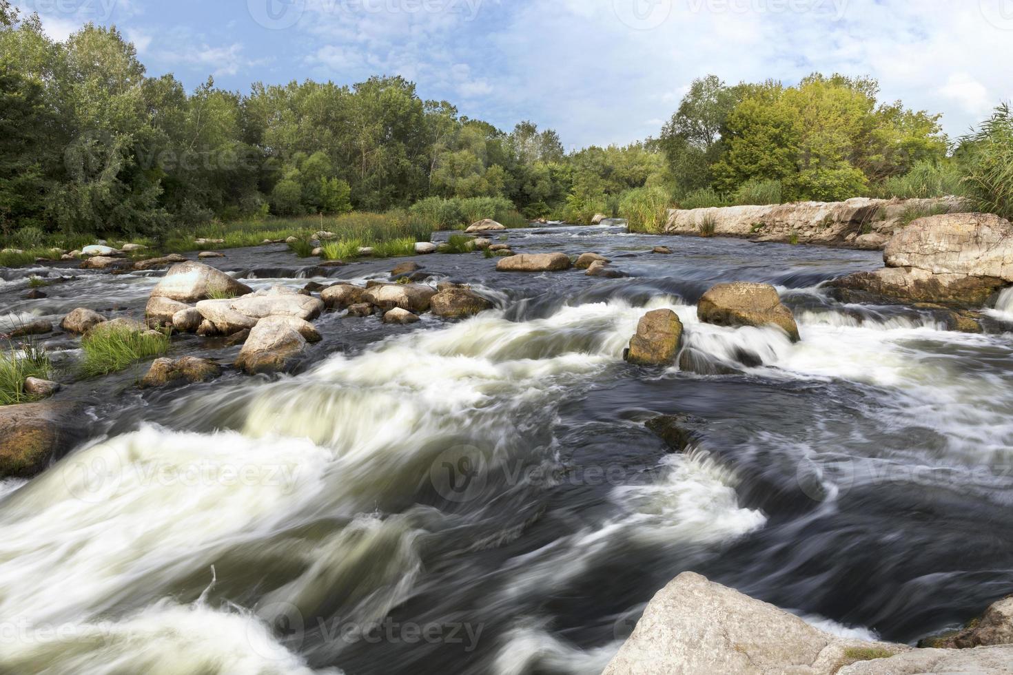 de snelle stroom van de rivier, rotsachtige kusten, stroomversnellingen, felgroene vegetatie en een bewolkte blauwe zomerlucht foto