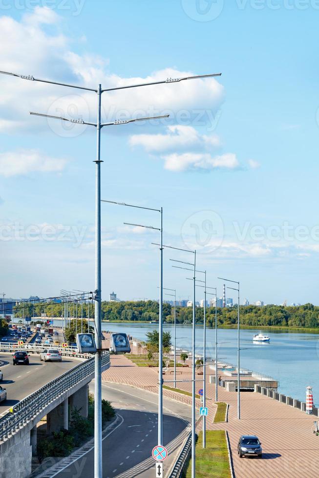 het ritme van hoge moderne lantaarnpalen aan de oever van de rivier tegen de achtergrond van een blauwe lucht met wolken. foto